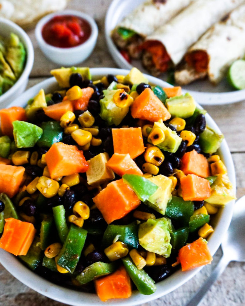 Close up of papaya black bean salad with tacos in the background