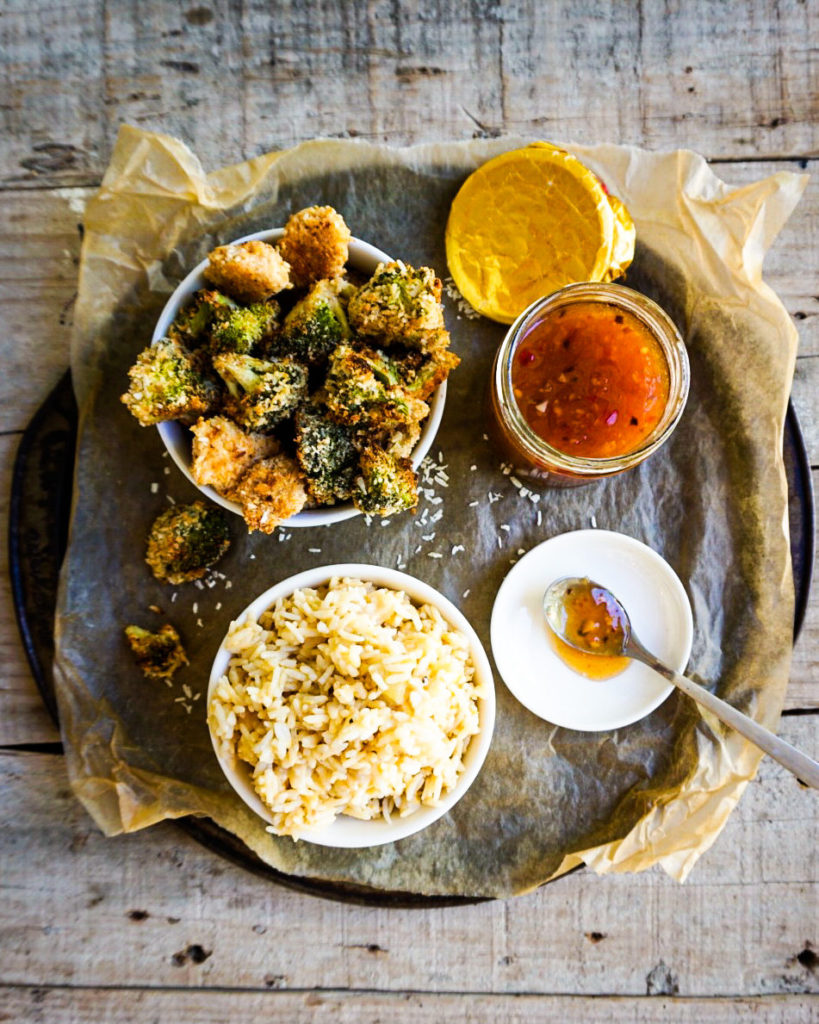 platter of broccoli and chicken, a bowl of rice and a jar of sweet chili sauce