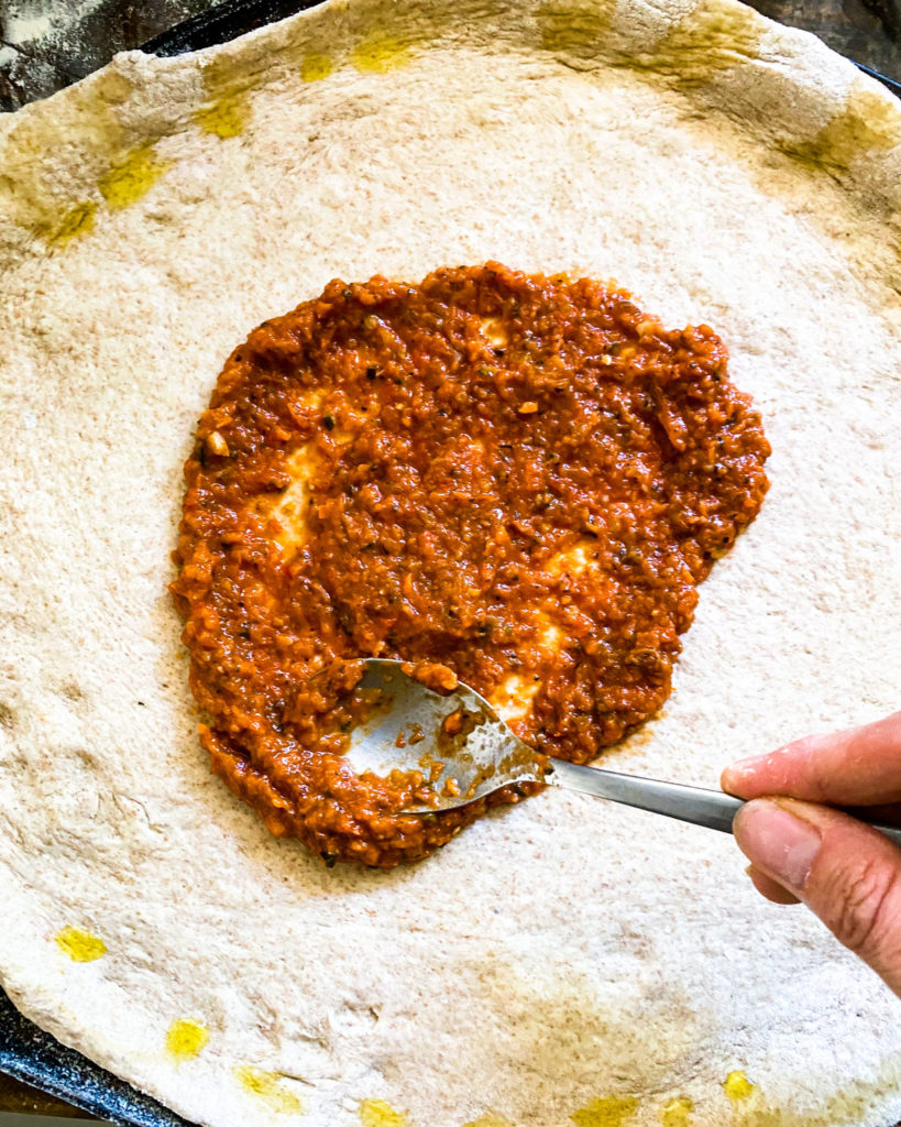 spreading sauce on the rolled out pizza dough