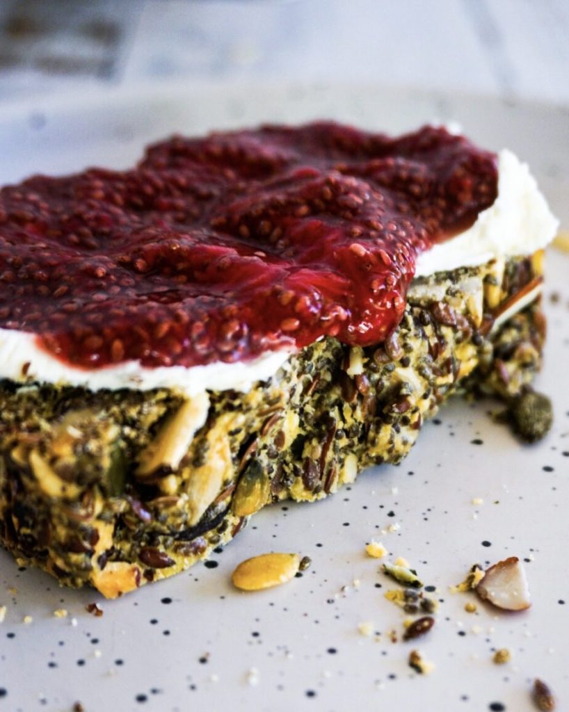 a slice of nuts and seeds bread with cream cheese and chia jam