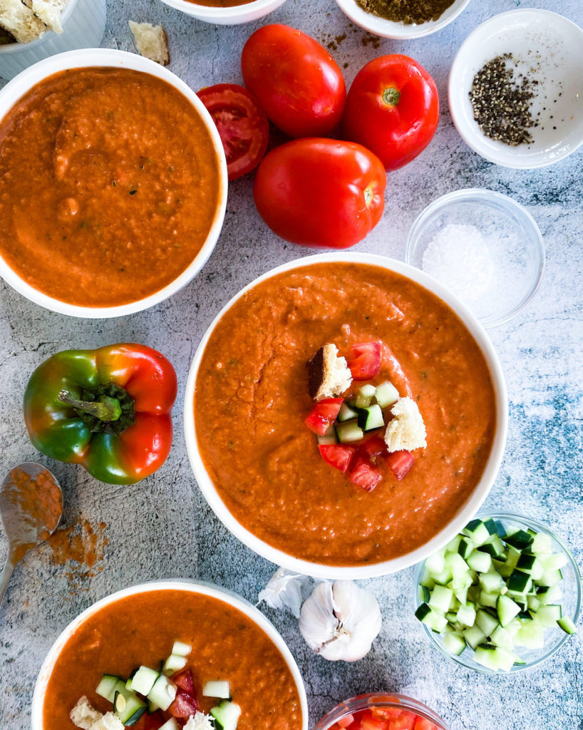 close up bowls of gazpacho and garnishing on the side
