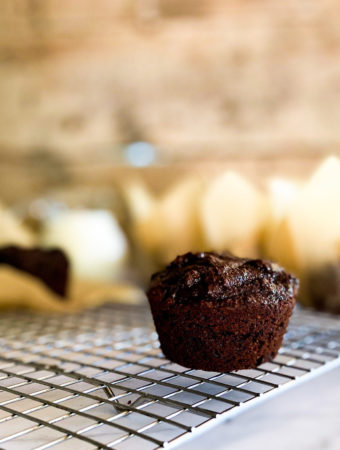 Brownie muffins on a cooling rack with many muffins in its wrapper in the background