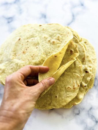 a hand going through a stack of fresh whole wheat tortillas