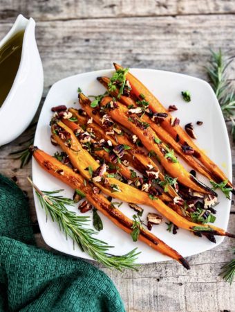 Roasted carrots on a plate topped with pecan herb crumble and maple glaze on the side